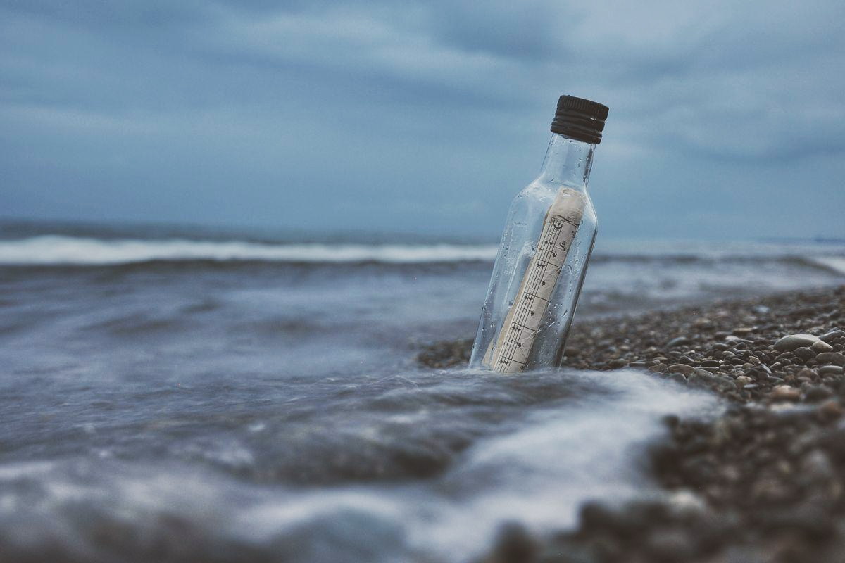 A glass bottle with a message inside, resting in the surf on a pebble beach