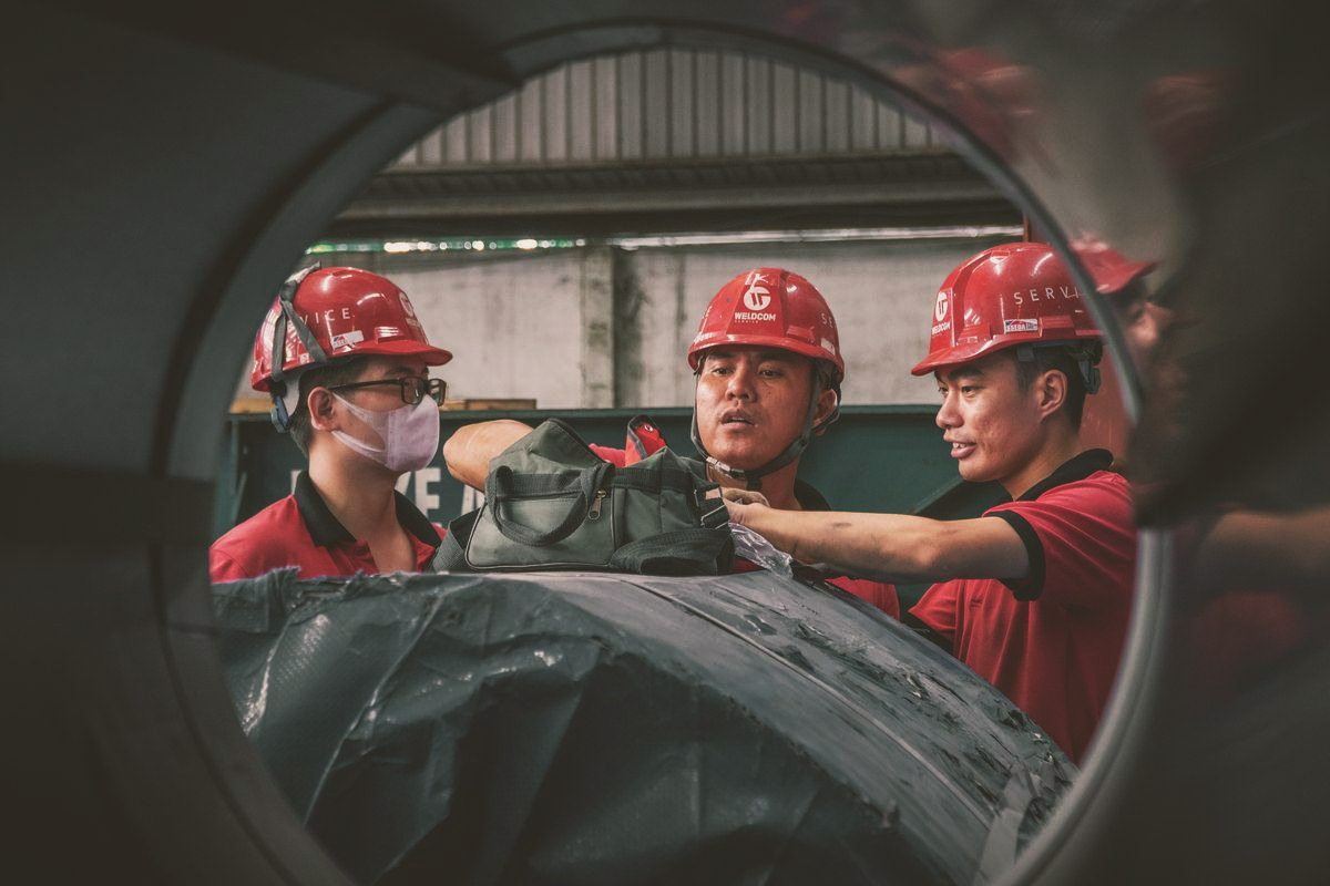 Three workers in hard hats and safety gear collaborating inside a factory