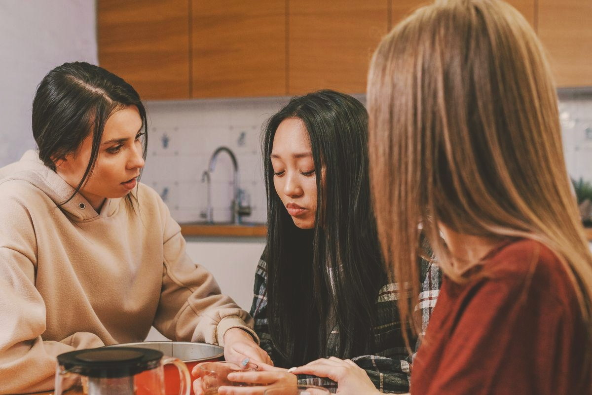 Three women at a kitchen table with tea, one listening closely