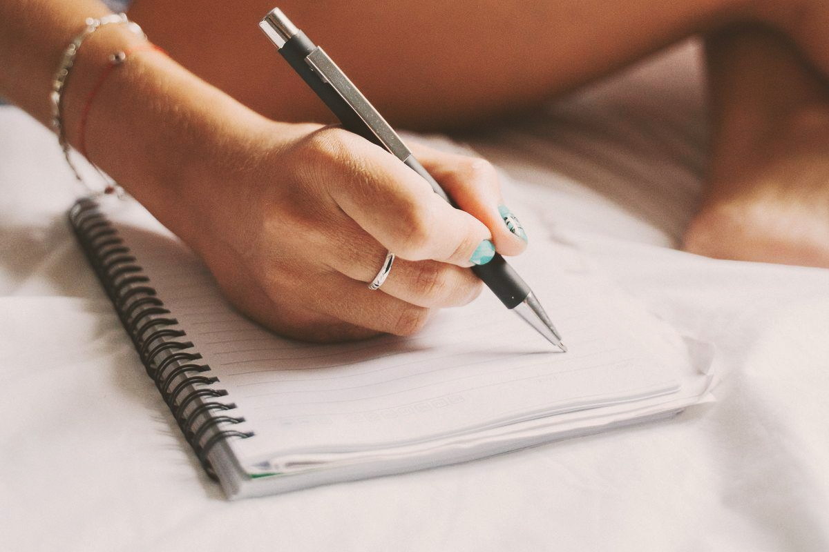 A hand writing in a spiral-bound notebook, pen in hand