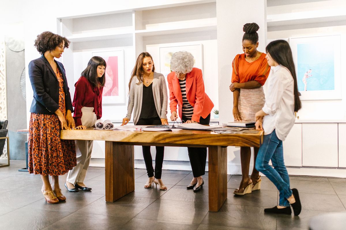 Six women reviewing plans around a wooden table in a bright office studio